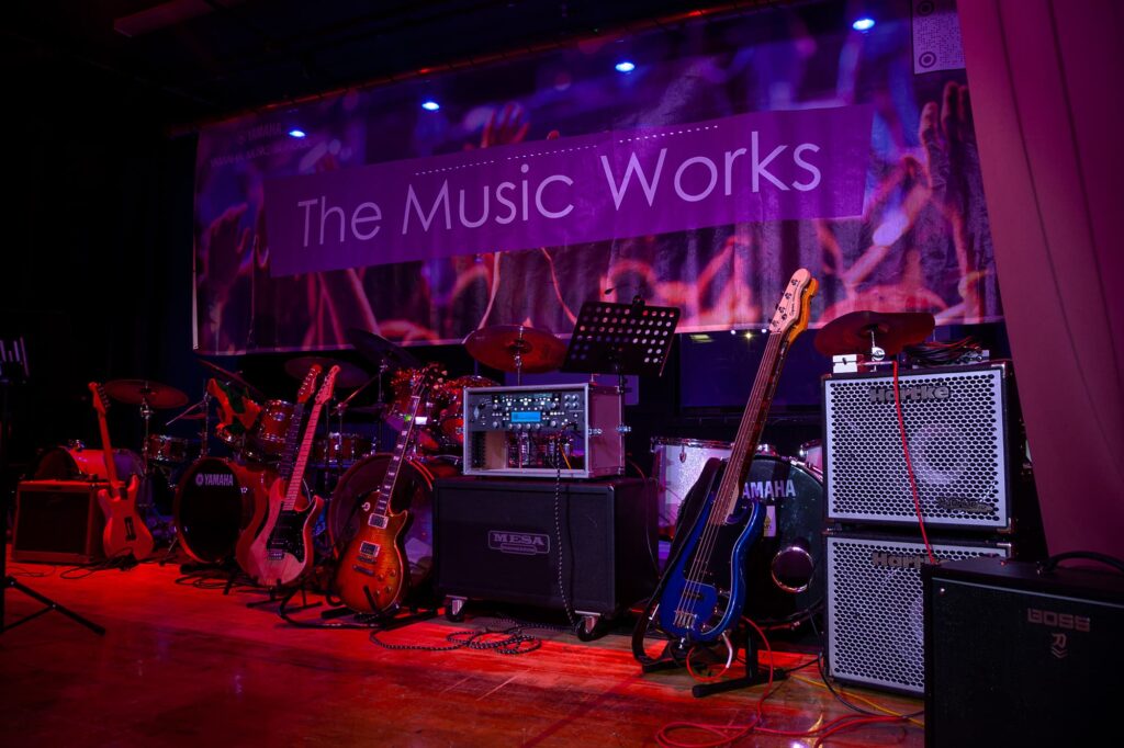 A dramatic image of a stage filled with pro music equipment, ready for a student and teacher live performance to parents.