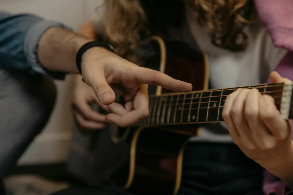 Close-up of a guitar teacher pointing to finger placement on the fretboard during a lesson.