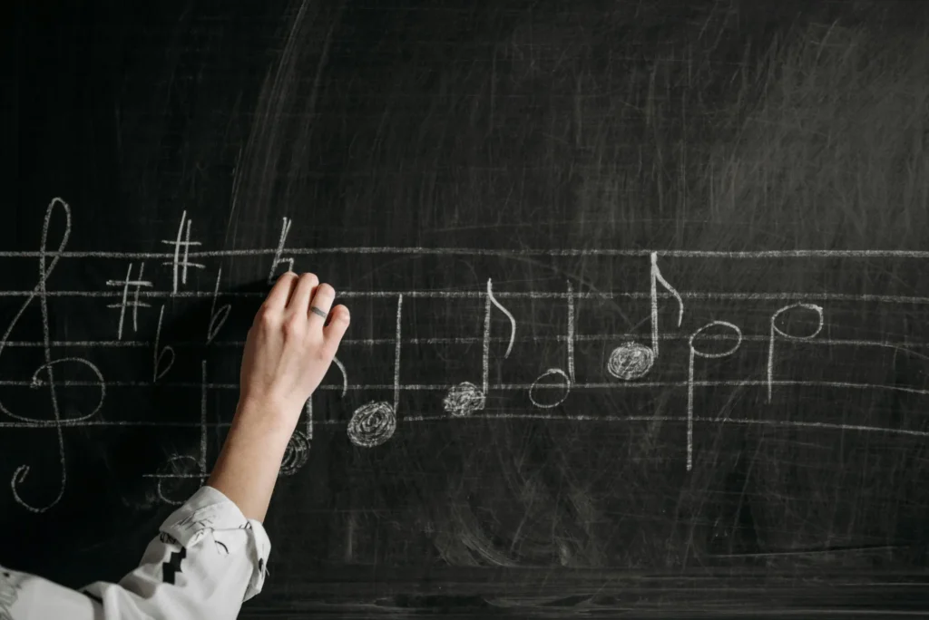 A hand drawing musical notes and sharp symbols on a blackboard with white chalk