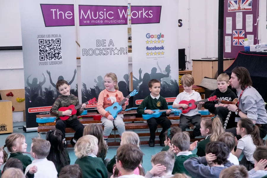 Children playing guitars and a musician performing on a cajón during a school music workshop led by The Music Works.