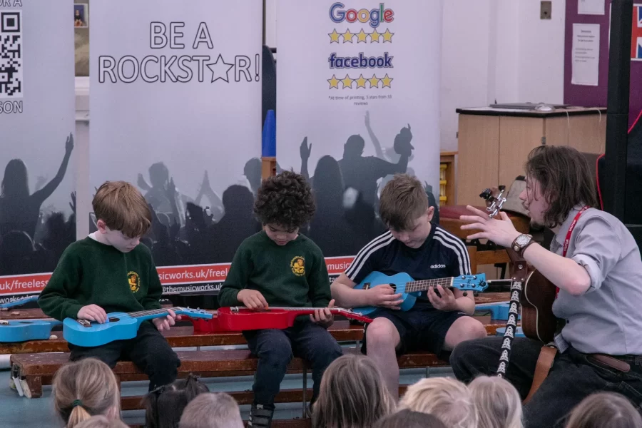 Children learning to play guitars during a school music workshop, guided by an instructor from The Music Works.