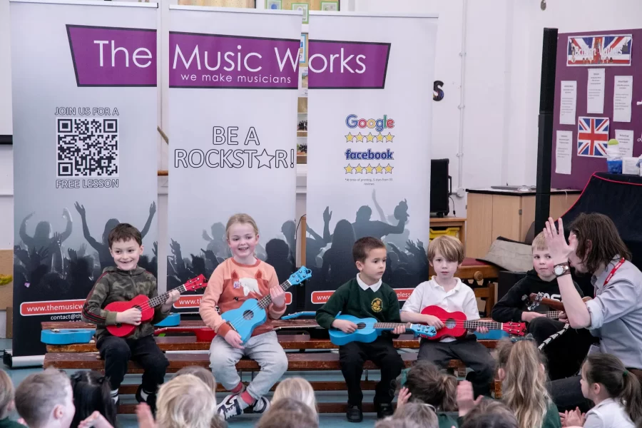 A group of children playing guitars during a school music workshop led by an instructor from The Music Works.