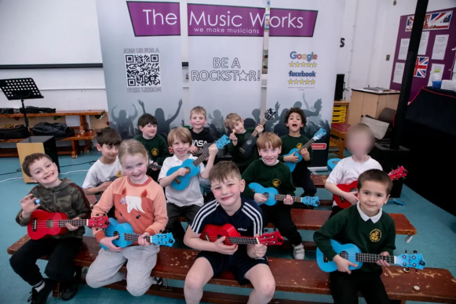 A group of happy children holding colorful ukuleles after participating in a school music workshop by The Music Works.