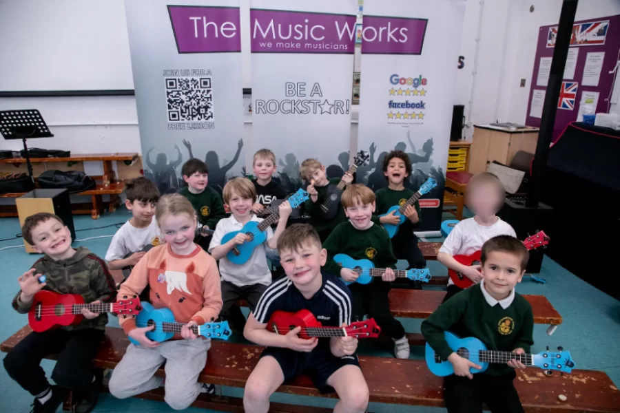 Smiling students holding guitars and ukuleles during a school music workshop hosted by The Music Works.