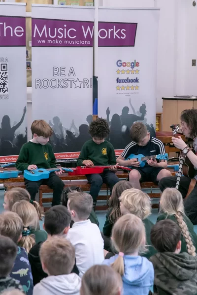Children learning to play guitars in a school music workshop, guided by an instructor from The Music Works.