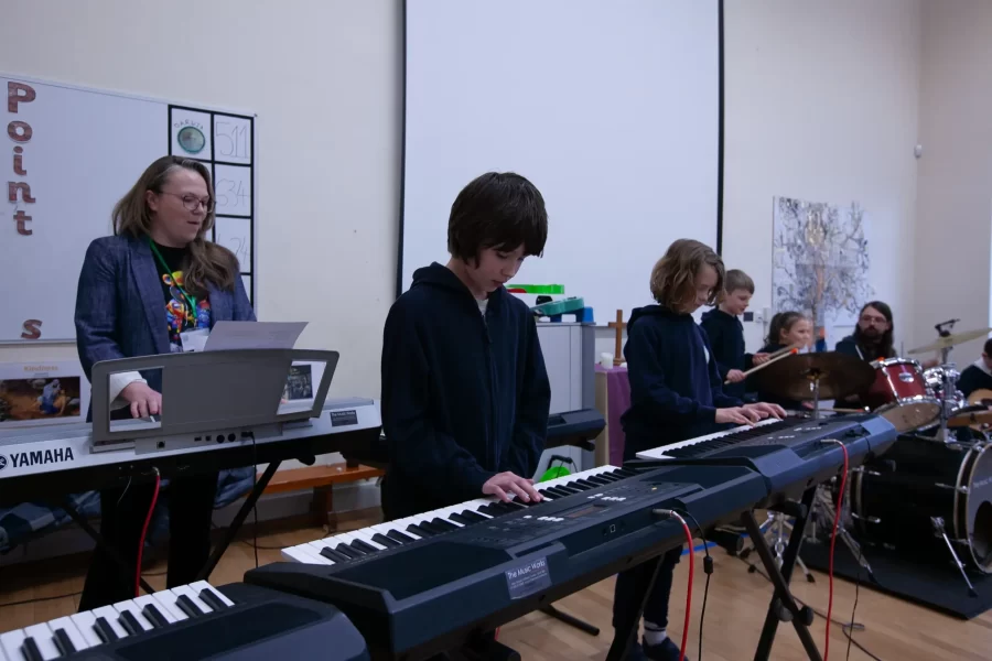 A young boy and girl playing electronic keyboards while a music teacher watches