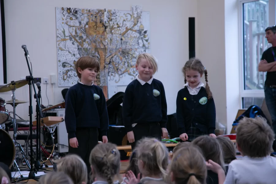 Three young students stand in front of an audience after a school music performance.